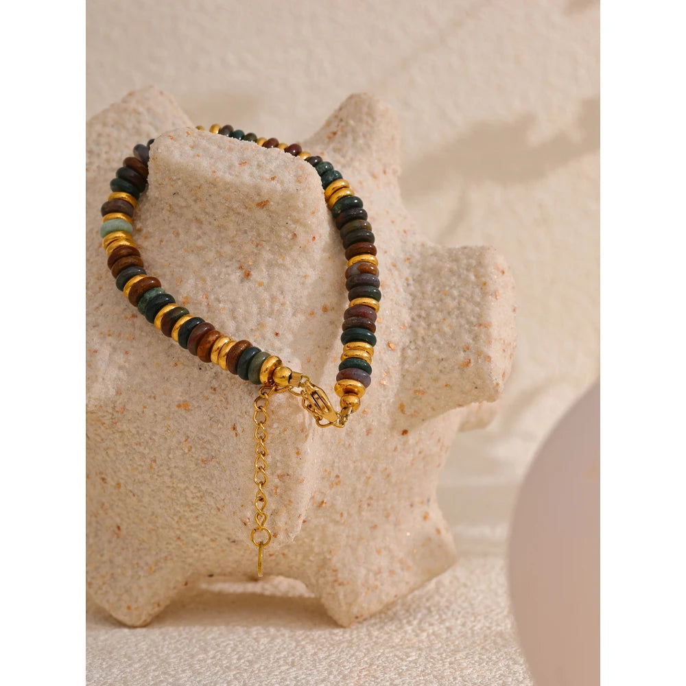 Multicoloured beaded bracelet with a gold chain on a textured beige surface