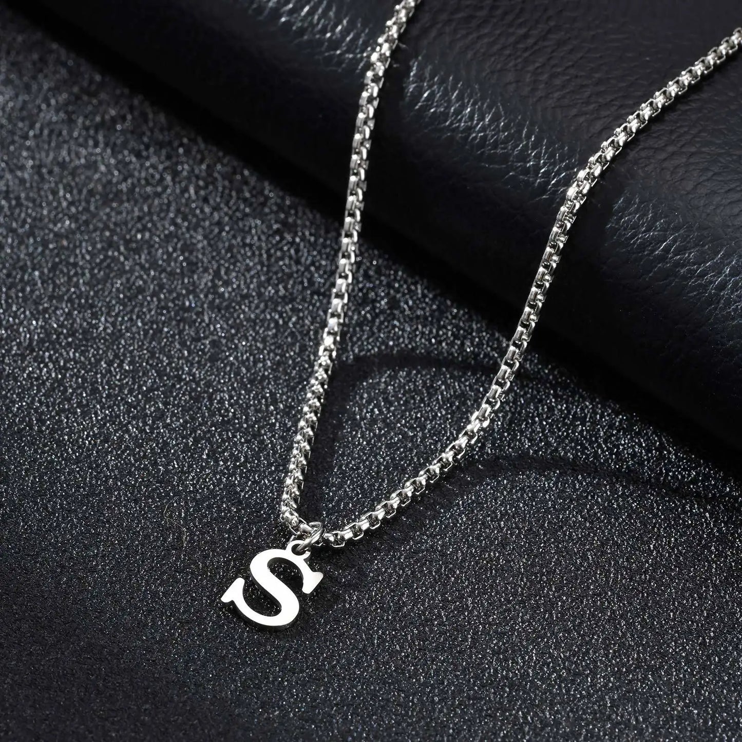 Silver necklace with a 'S' pendant on a black textured surface