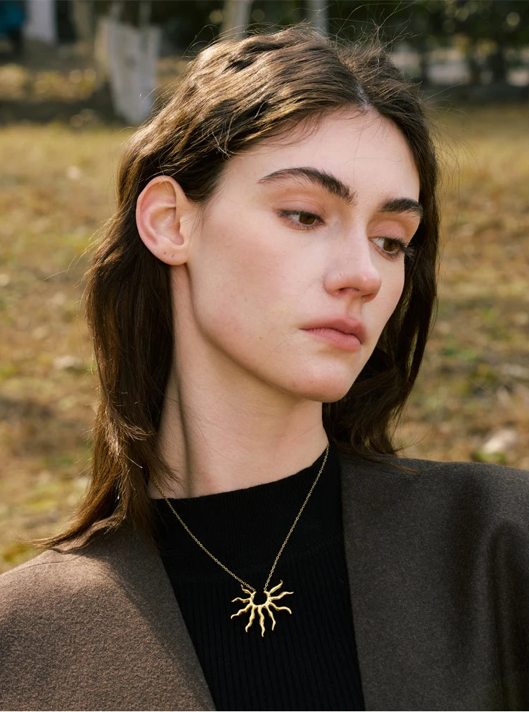 Woman wearing a gold necklace with a sun design outdoors