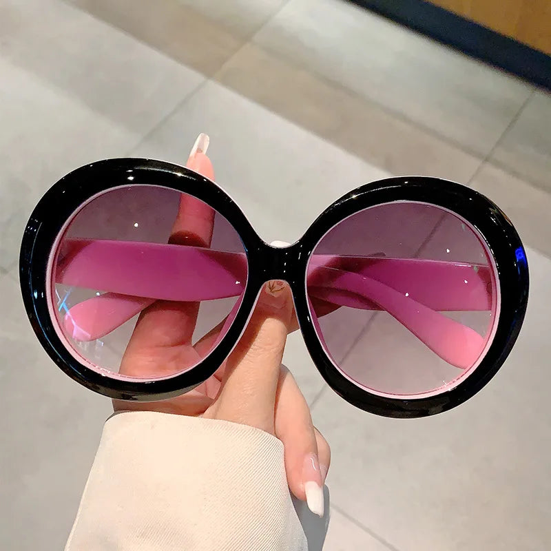 Sunglasses with black frames and pink lenses held by a hand.