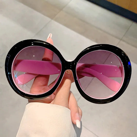 Sunglasses with black frames and pink lenses held by a hand.