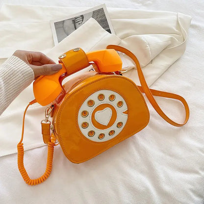 Orange phone-shaped handbag with a heart design on a white surface