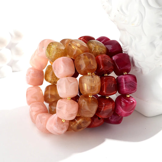 Set of three beaded bracelets in pink, gold, and red on a white surface.