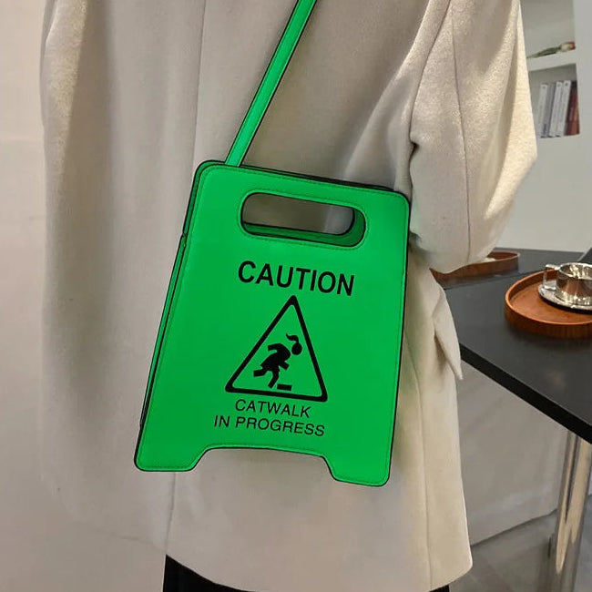 Person wearing a green bag with a 'Caution: Catwalk in Progress' sign.