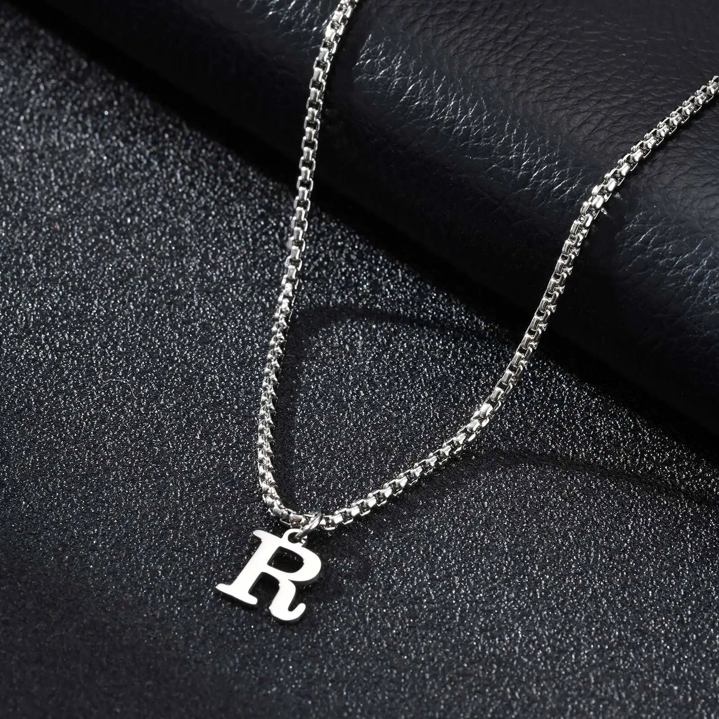 Silver necklace with a 'R' pendant on a black textured surface