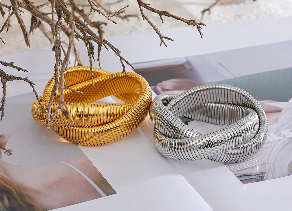 Two metallic bracelets, one gold and one silver, on a magazine with a blurred background.
