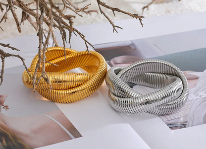 Two metallic bracelets, one gold and one silver, on a magazine with a blurred background.