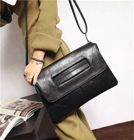 Person holding a black clutch bag with a plain background