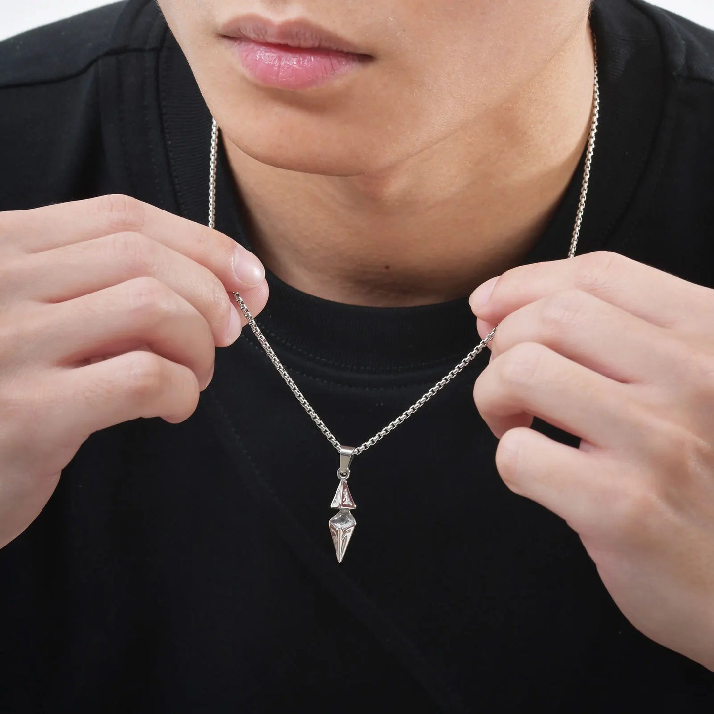 Person holding a silver necklace with a pendant against a black background