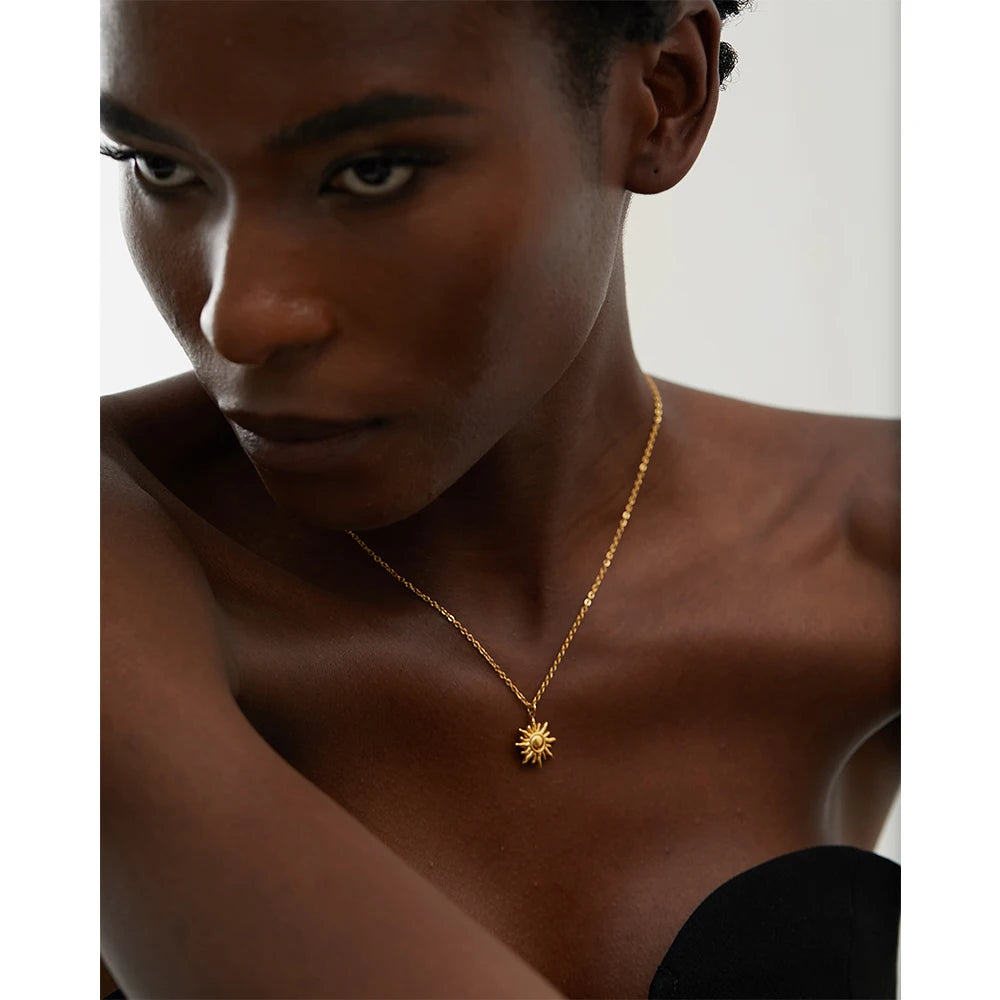 Woman wearing a gold necklace with a sun pendant against a neutral background