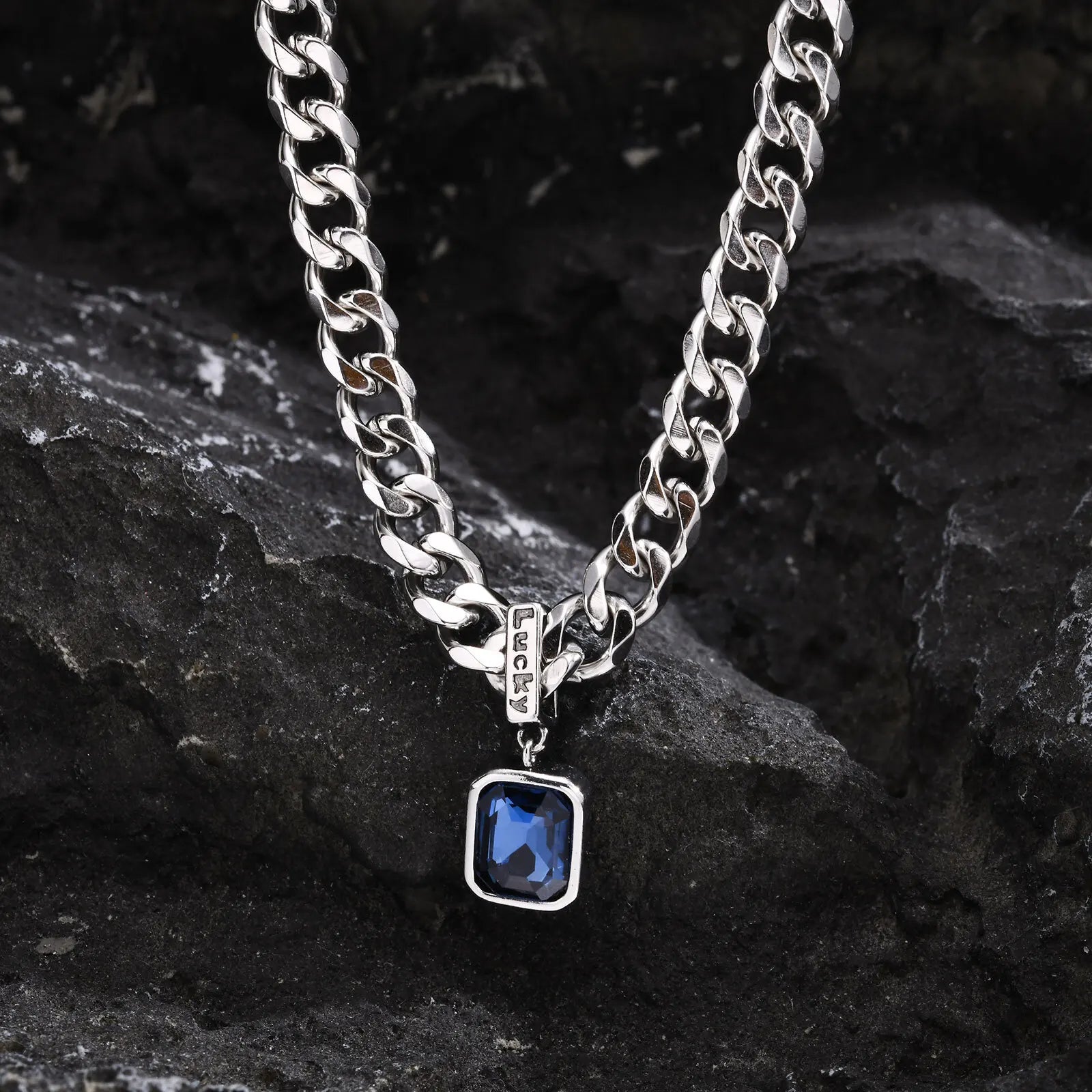 Silver chain necklace with a blue pendant on a dark stone surface