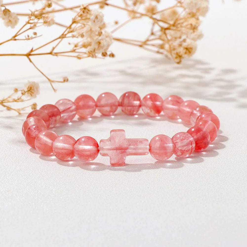 Pink beaded bracelet with a cross charm on a light background with dried flowers.