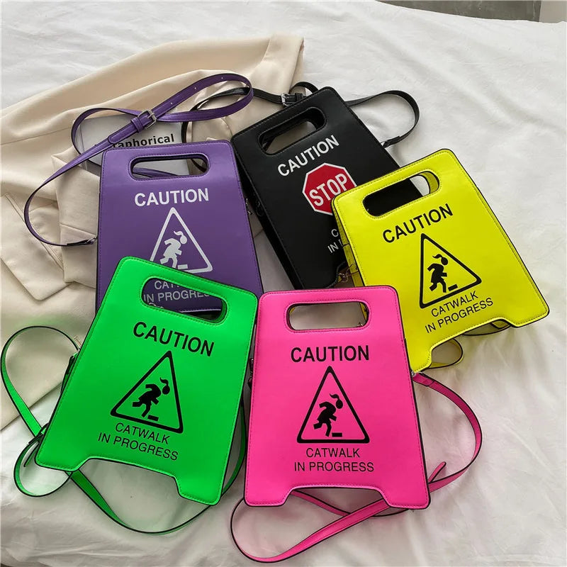 Five colourful bags with 'Caution: Catwalk in Progress' design on a white fabric background.