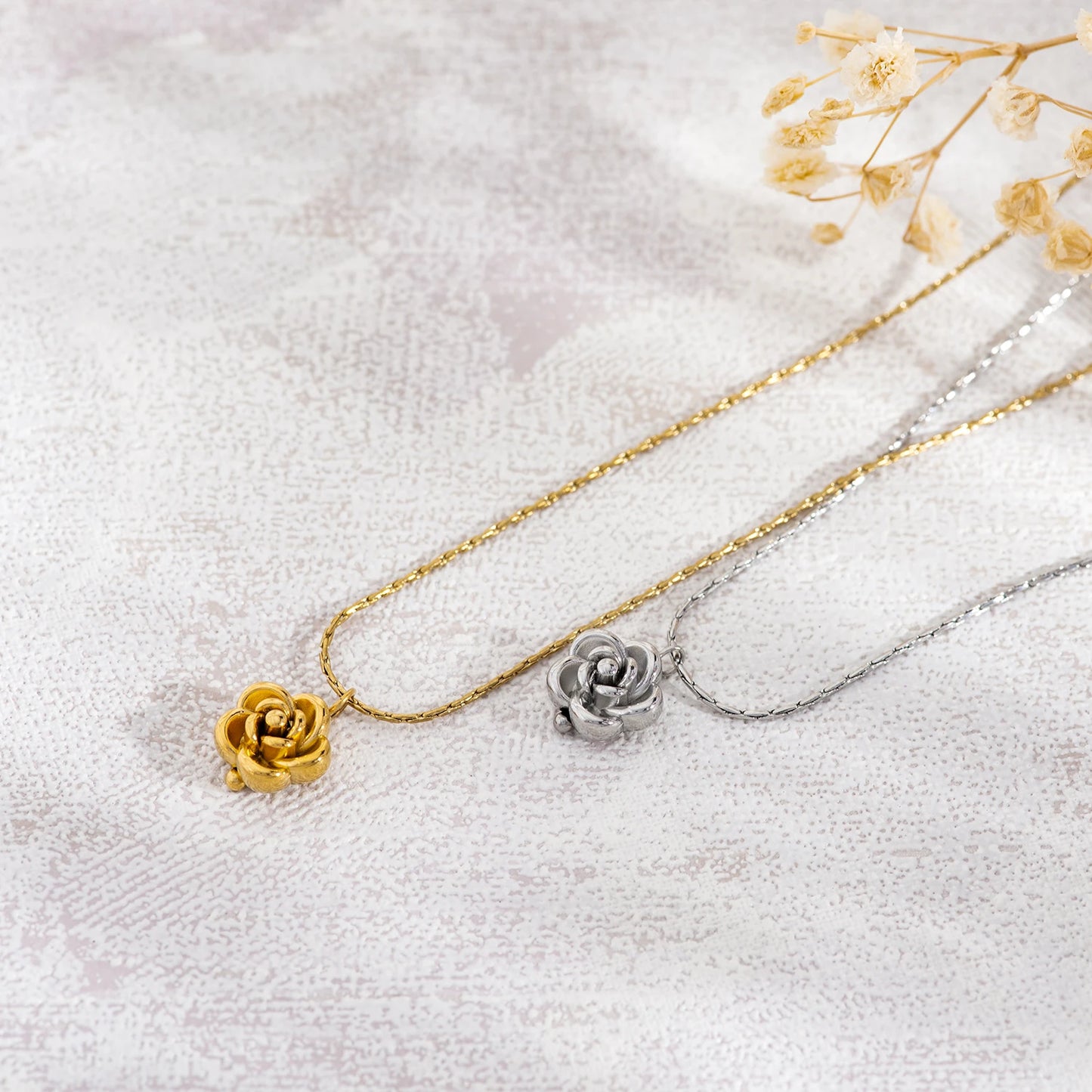 Two necklaces with rose pendants, one gold and one silver, on a light fabric background.