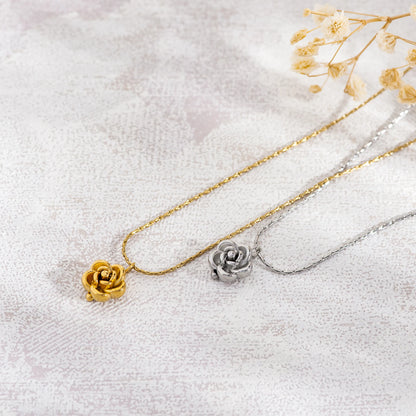 Two necklaces with rose pendants, one gold and one silver, on a light fabric background.