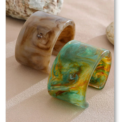 Two marbled cuff bracelets on a textured surface