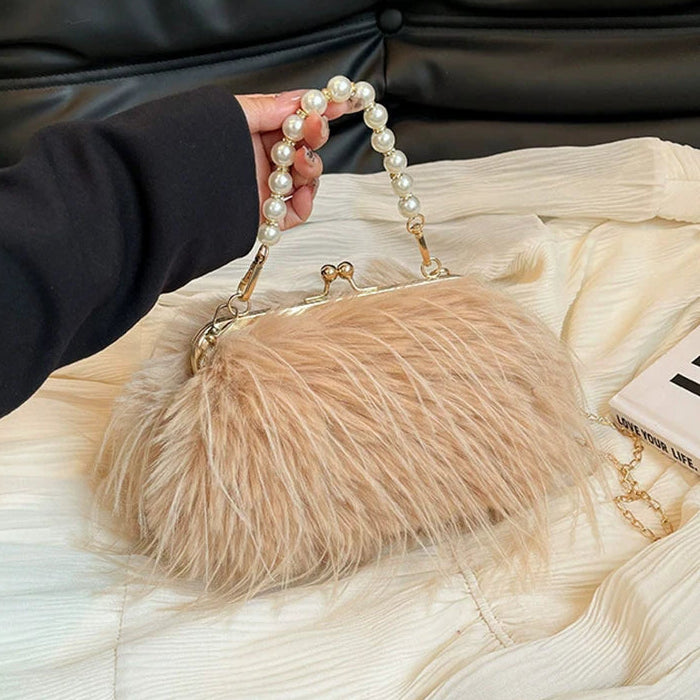 Beige feathered handbag with pearl handle held by a person on a textured surface.