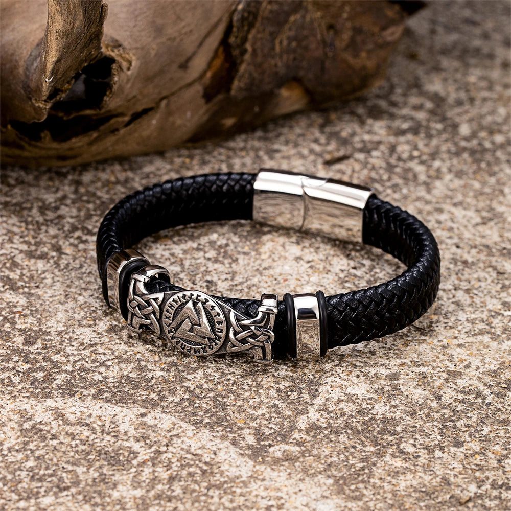 Black leather bracelet with silver clasp and decorative element on a textured surface