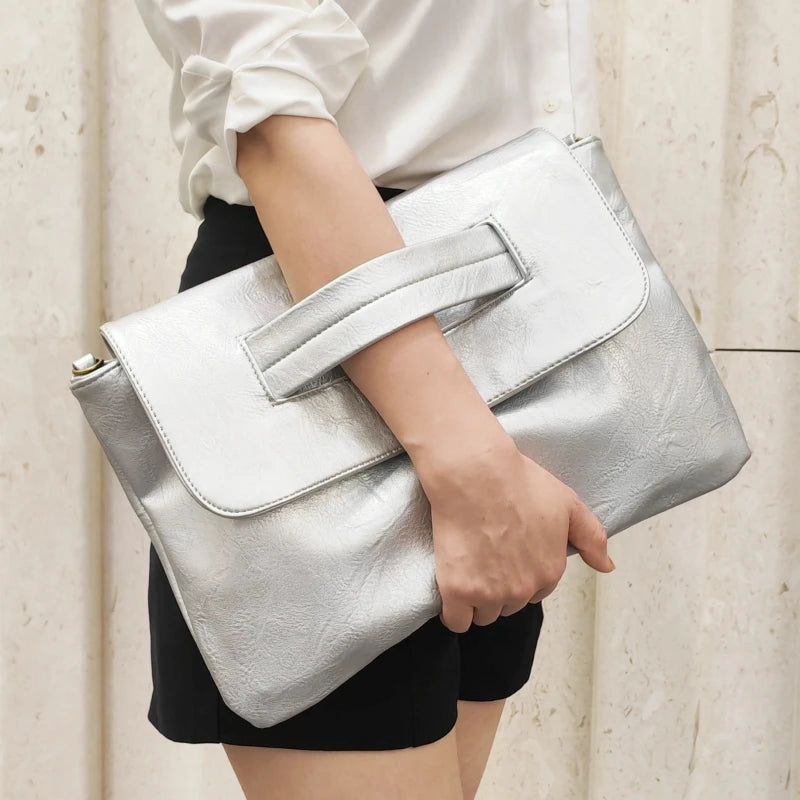 Person holding a silver clutch bag against a neutral background