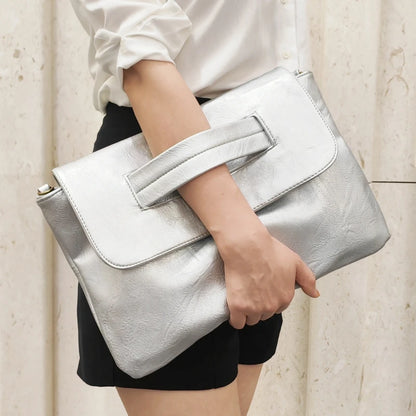 Person holding a silver clutch bag against a neutral background