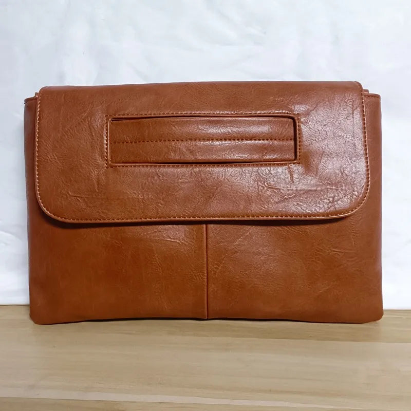 Brown leather clutch bag on a wooden surface with a white background