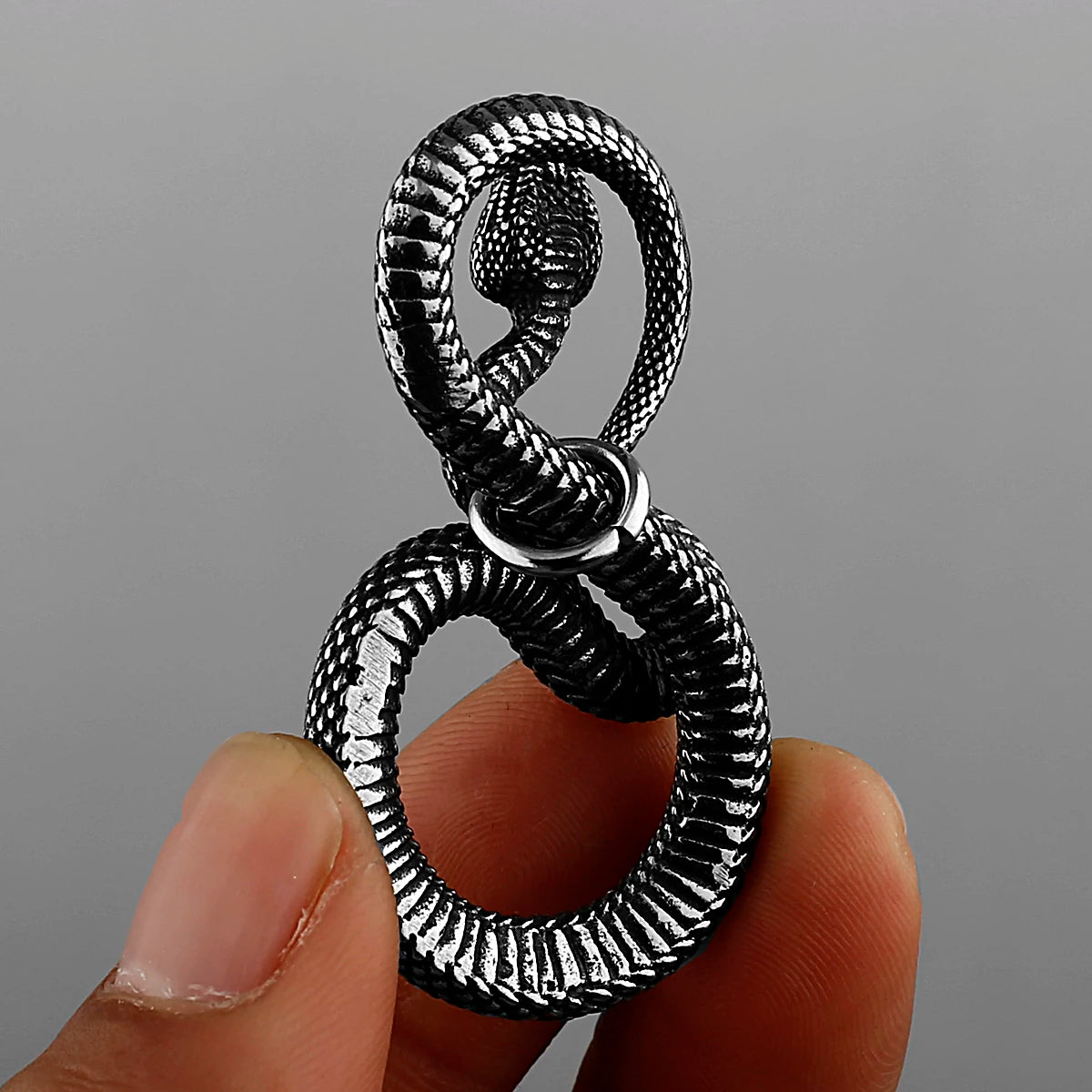 Silver pendant with intricate snake design held between fingers against a grey background