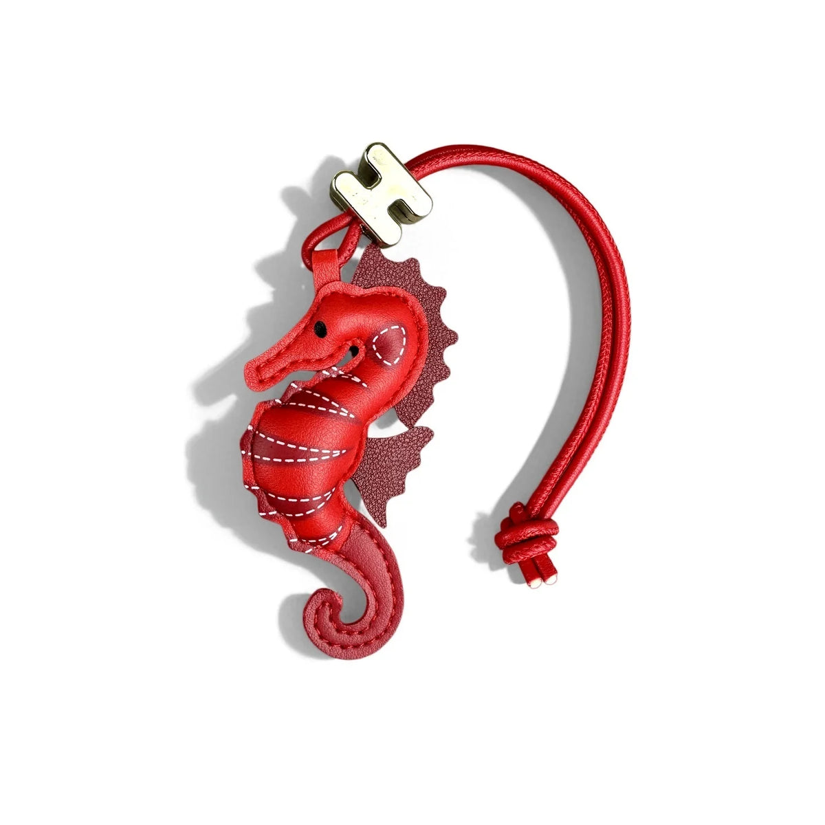 A red leather seahorse charm with white contrast stitching, attached to a matching red adjustable cord bracelet with a silver-toned H logo bead, shown on a white background.