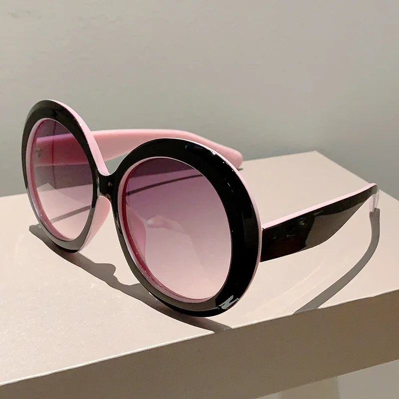 Sunglasses with pink lenses and black frames on a light surface.