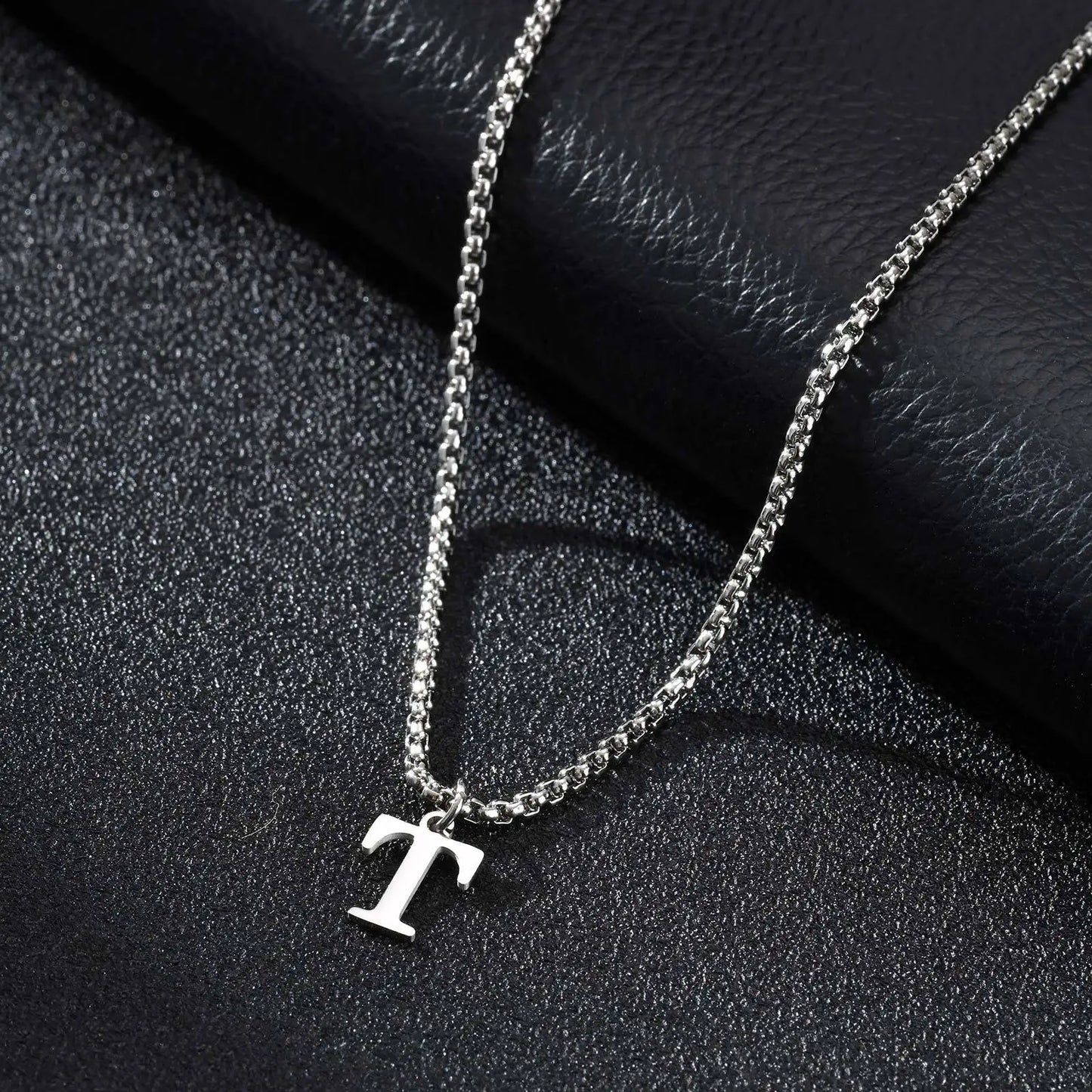 Silver necklace with a 'T' pendant on a dark textured surface