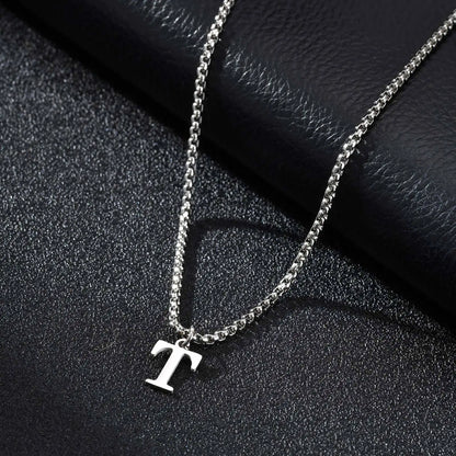 Silver necklace with a 'T' pendant on a dark textured surface