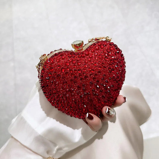 Red heart-shaped clutch bag with rhinestone details held by a hand against a light background