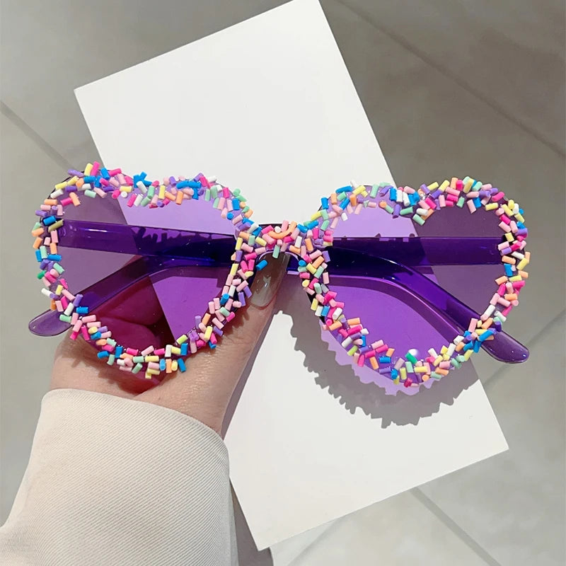 Sunglasses with colourful heart-shaped frames held by a hand on a white background