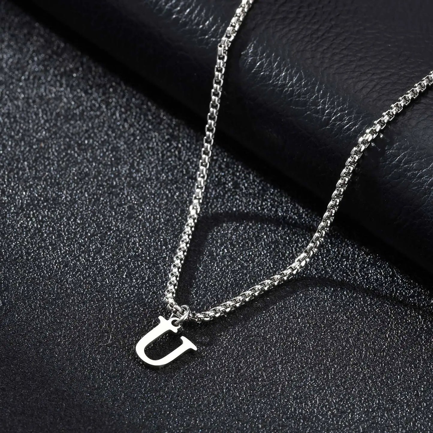 Silver necklace with a 'U' pendant on a black textured surface