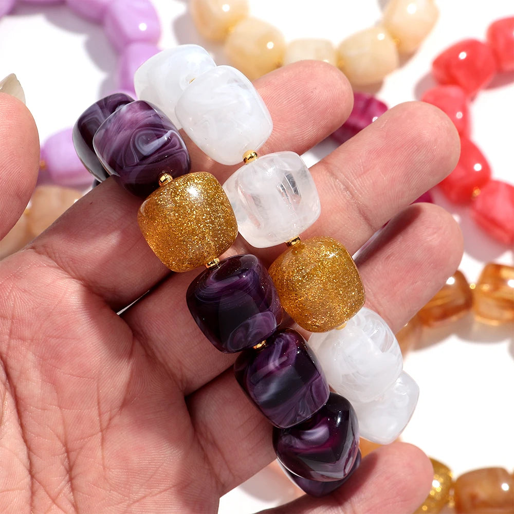 Hand holding a beaded bracelet with various coloured beads against a blurred background of more bracelets.