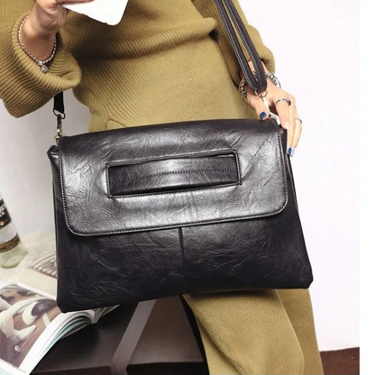 Person holding a black leather handbag with a bottle and magazine in the background