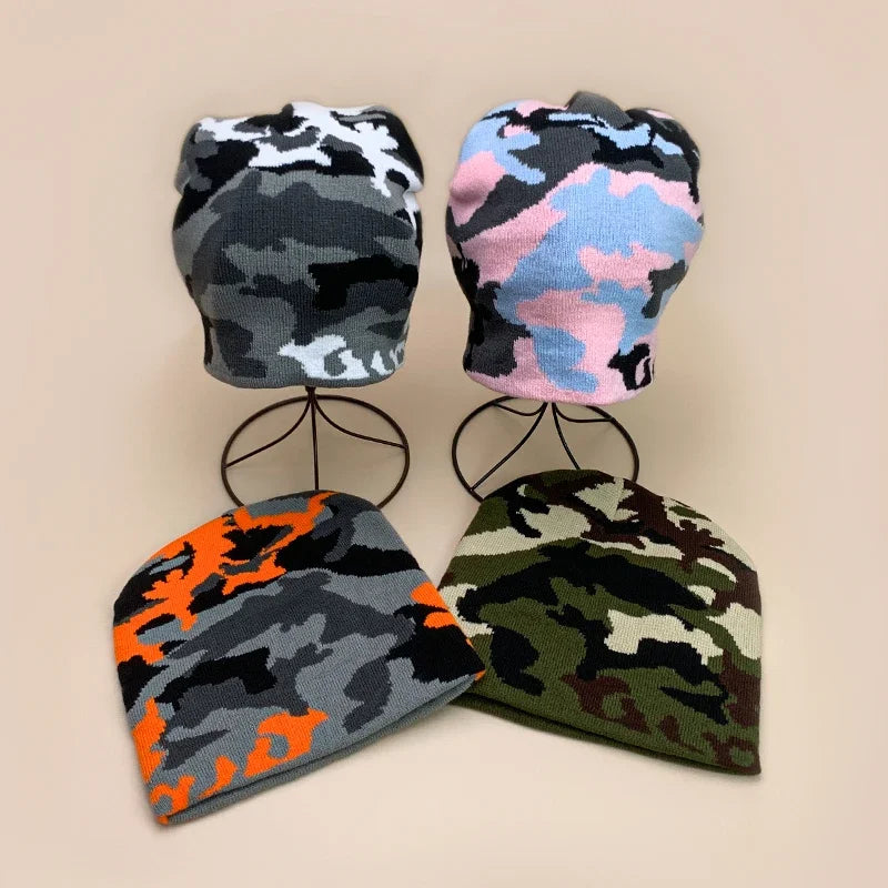 Four camouflage-patterned beanies on black stands against a beige background
