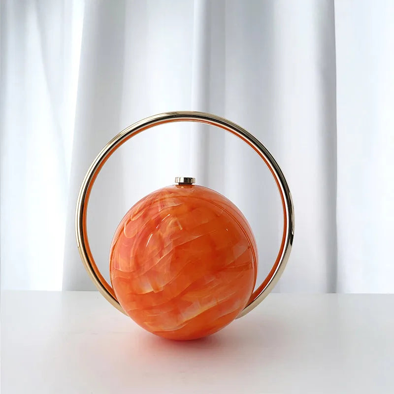 Orange spherical clutch bag with a gold circular frame on a white background