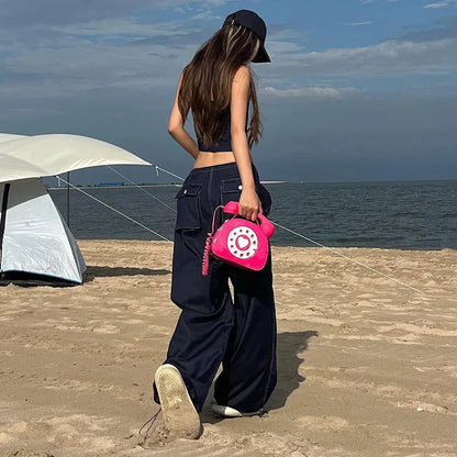 Person holding a pink phone-shaped bag on a beach with tents in the background