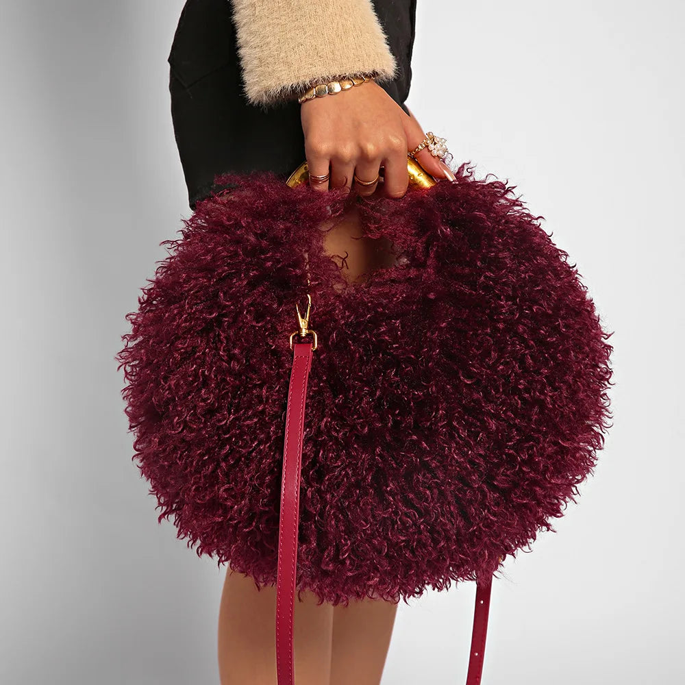 Maroon fuzzy handbag with a pink strap held by a person against a neutral background