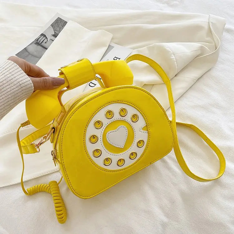 Yellow phone-shaped bag with a heart detail on a white surface