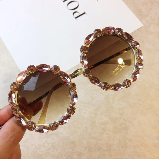 Sunglasses with decorative frame held by a hand on a beige background