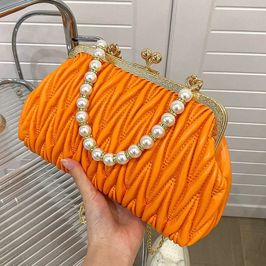 Orange clutch bag with pearl detailing held by a hand against a neutral background