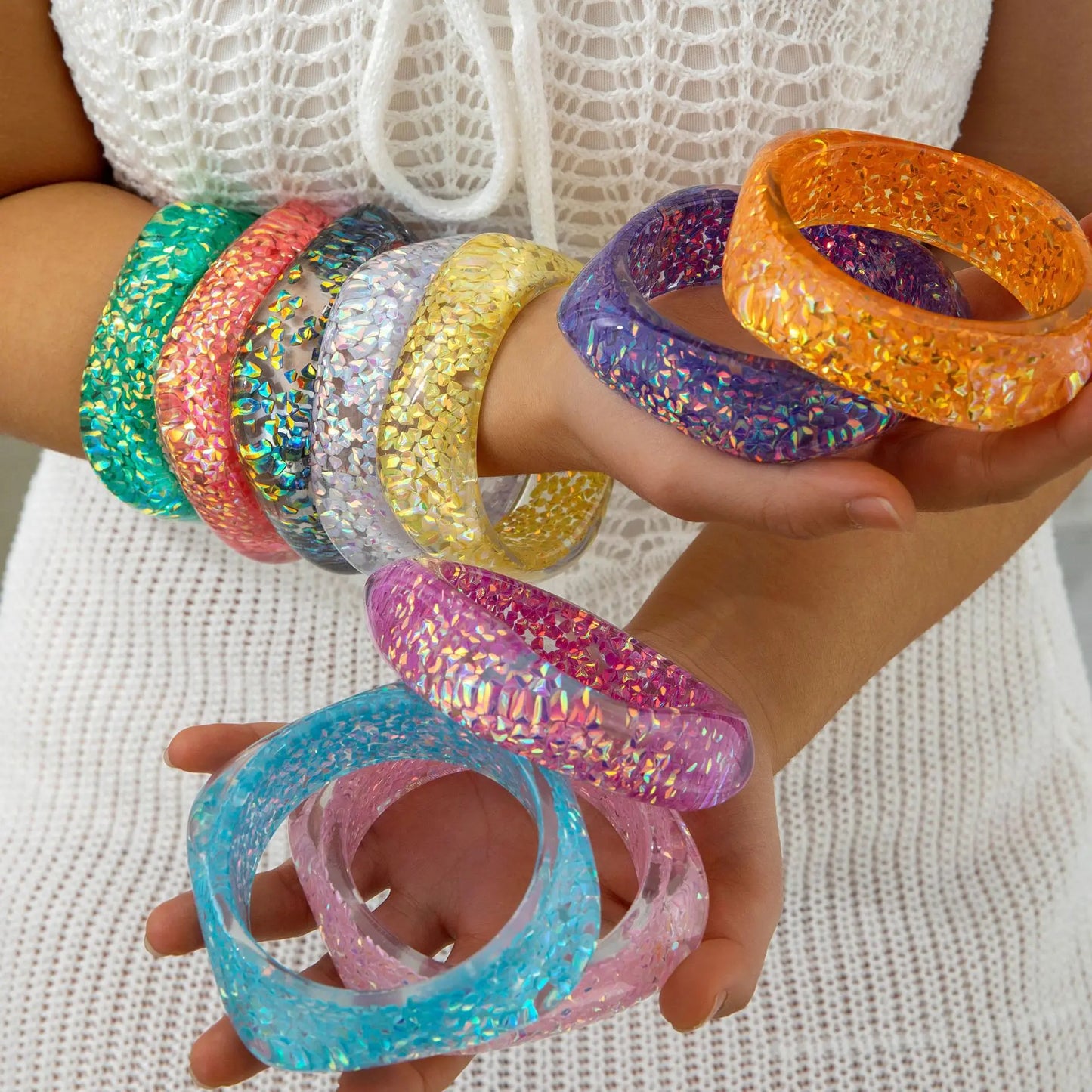 Colourful glittery bangles on a person's wrist against a white background