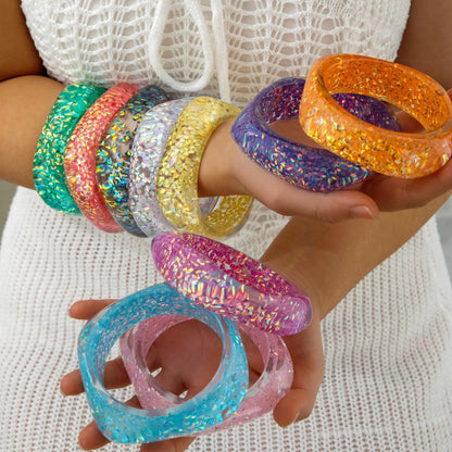Colourful glittery bangles on a person's wrist against a white background