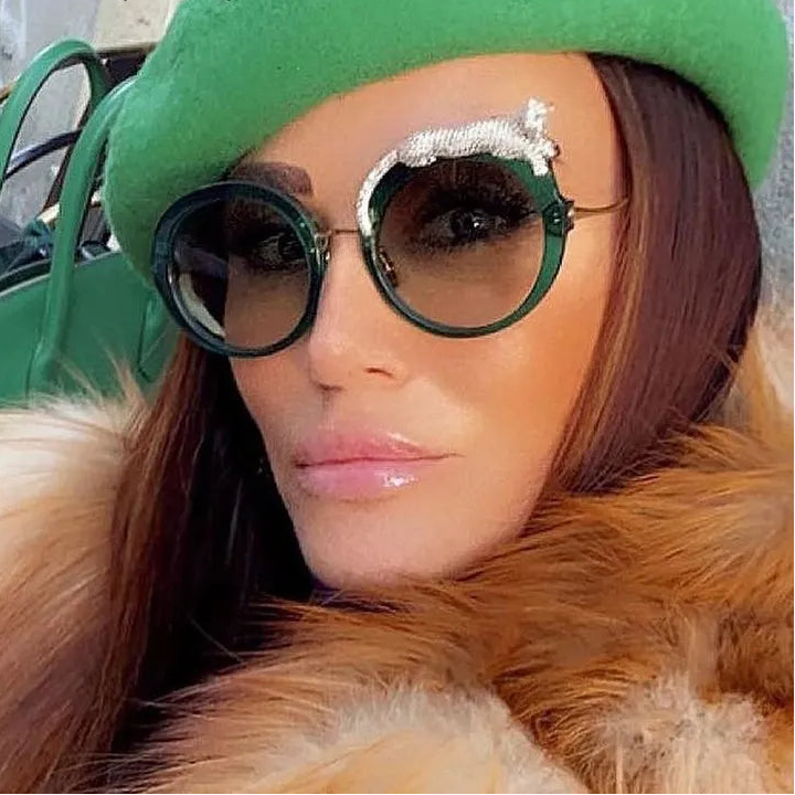 Person wearing a green beret and fur coat with decorative sunglasses