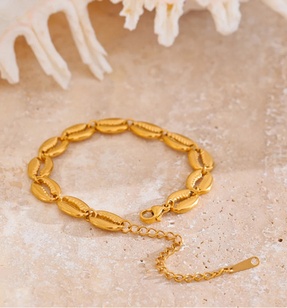 Gold bracelet on a textured surface with a shell in the background