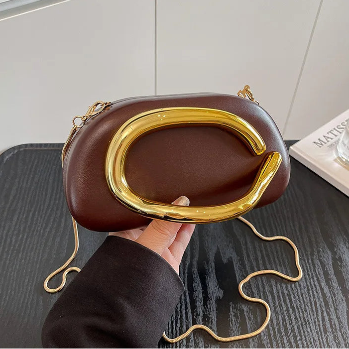 Brown handbag with gold accents held by a hand on a neutral background