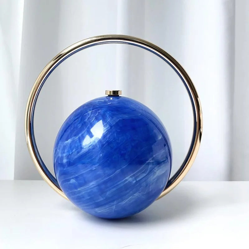 Blue spherical clutch bag with a gold circular frame on a white background