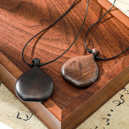 Two wooden pendants on black cords on a wooden surface with calligraphy.