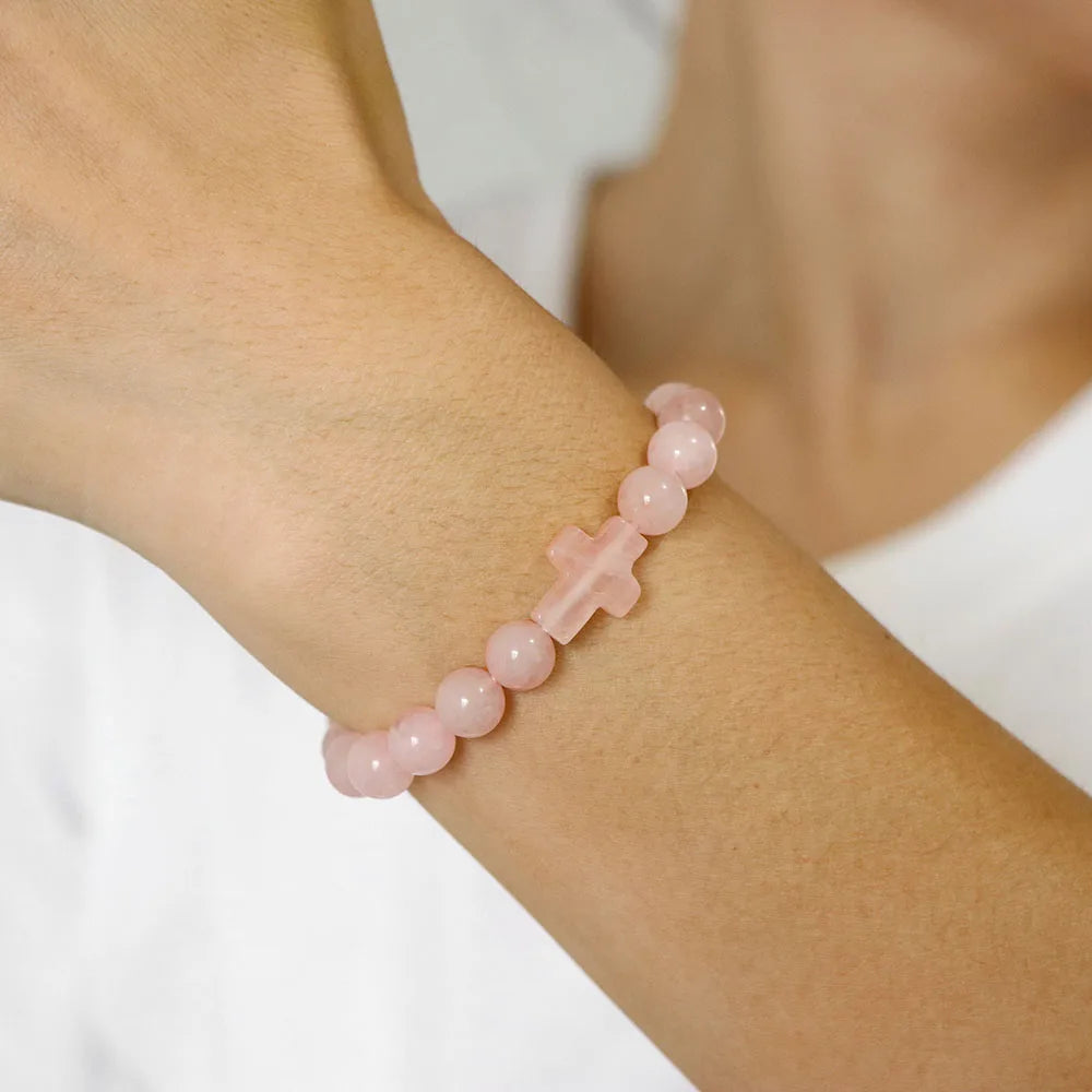 Pink beaded bracelet with a cross on a wrist against a white background